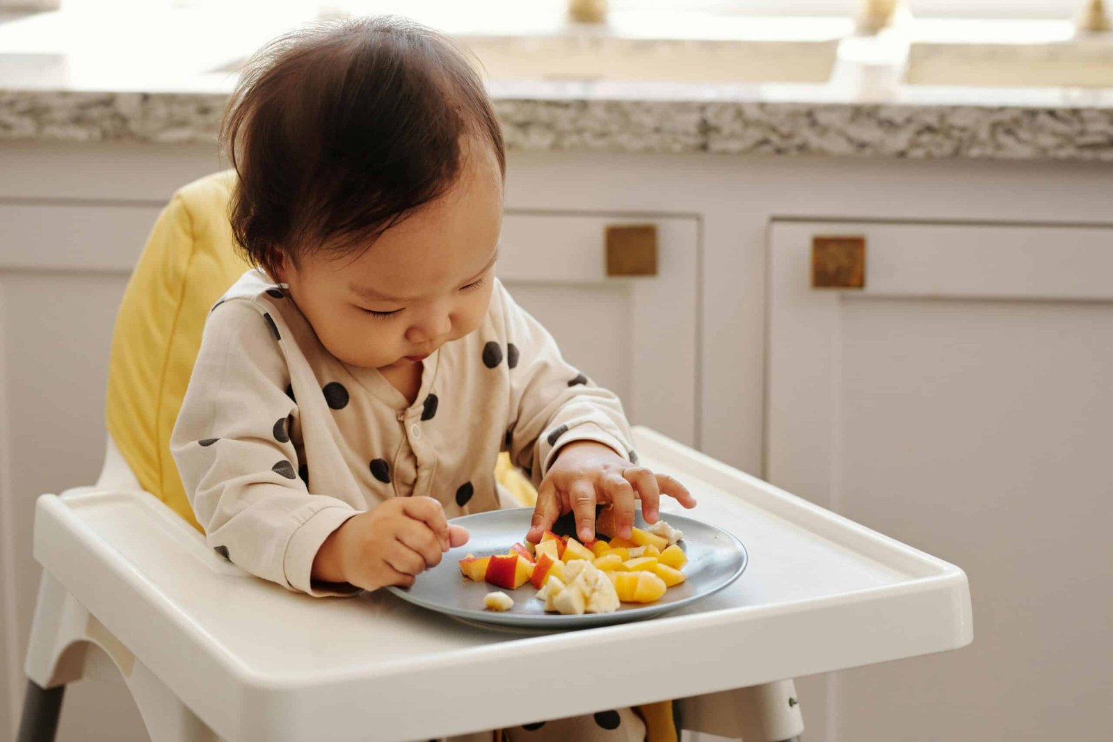 A cute toddler in a polka dot outfit enjoying a healthy fruit snack indoors.